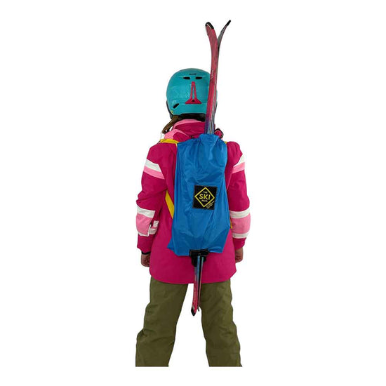 Child wearing a pink jacket, green pants, blue helmet, and carrying a blue backpack with skis on a white background