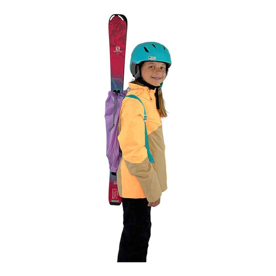 A child wearing a turquoise helmet and a yellow and beige ski jacket, shown from the side while carrying a Lavender Ski Pack with Teal Straps with skis on a plain white background.