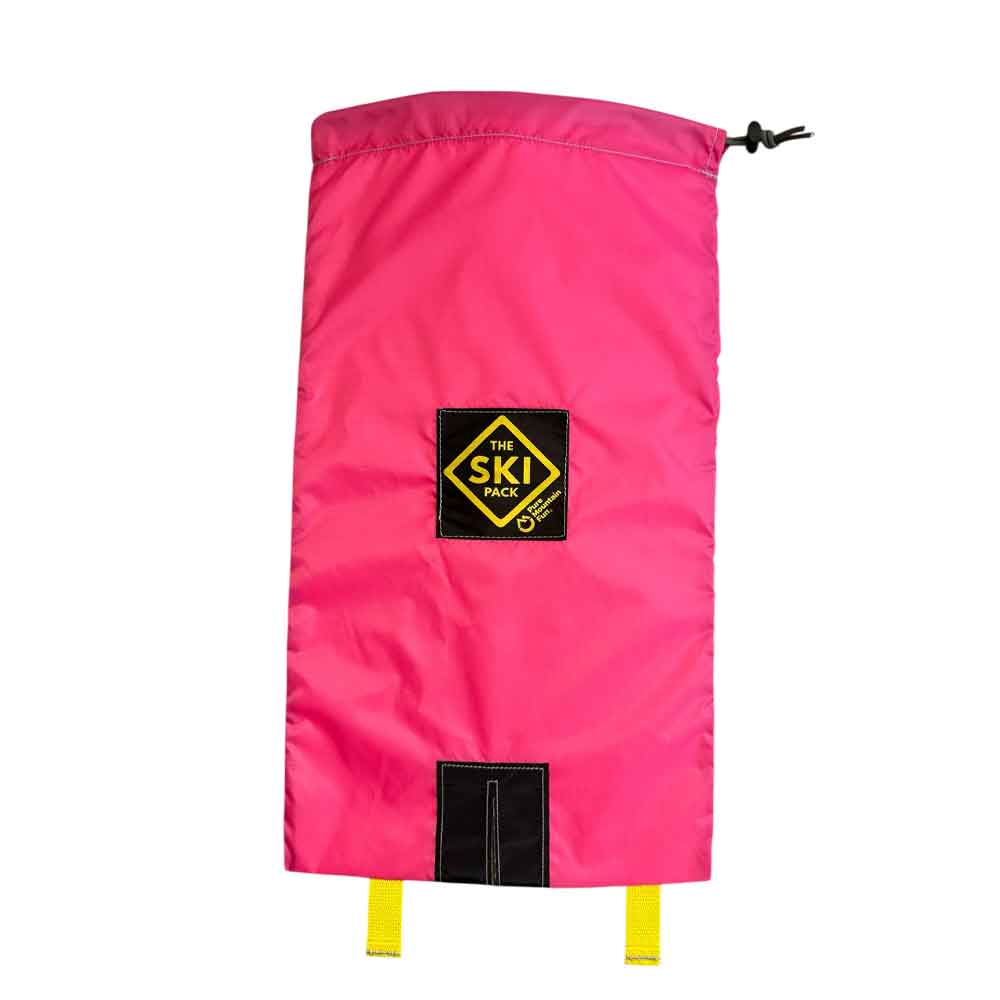A bright pink ski bag with a black drawstring closure, a black and yellow 'The Ski Pack' logo patch in the center, and a black hook-and-loop patch near the bottom with two yellow straps hanging from it, shown against a plain white background.