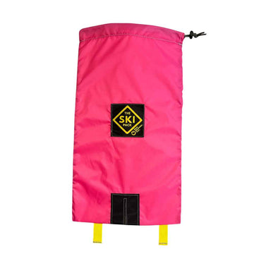 A bright pink ski bag with a black drawstring closure, a black and yellow 'The Ski Pack' logo patch in the center, and a black hook-and-loop patch near the bottom with two yellow straps hanging from it, shown against a plain white background.