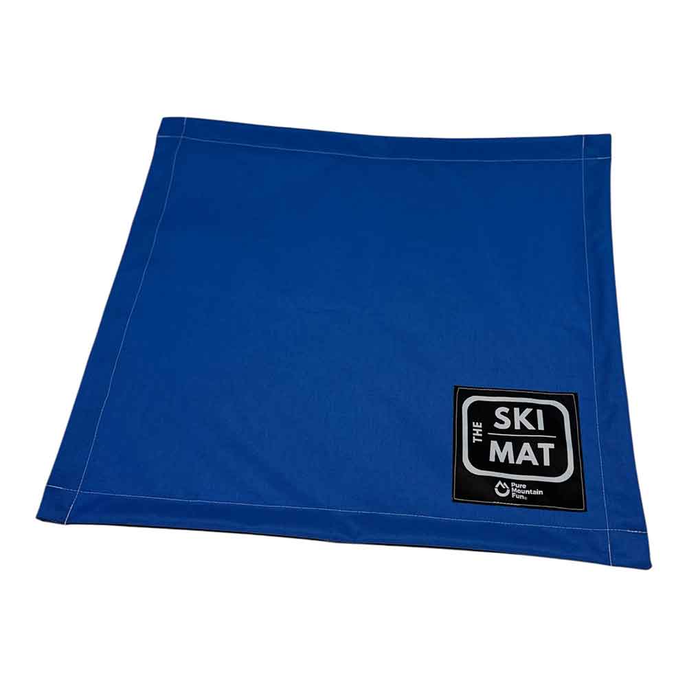 A royal blue ski mat with white stitching and a black square logo patch on the bottom right corner that reads 'THE SKI MAT'.