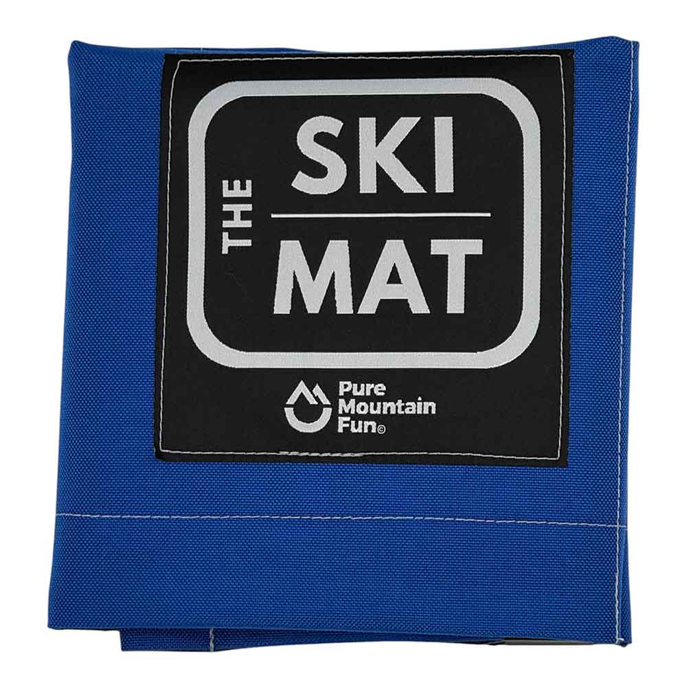 A folded blue ski mat with a black square label on the front that reads 'THE SKI MAT' and shows the 'Pure Mountain Fun' logo, photographed on a white background.
